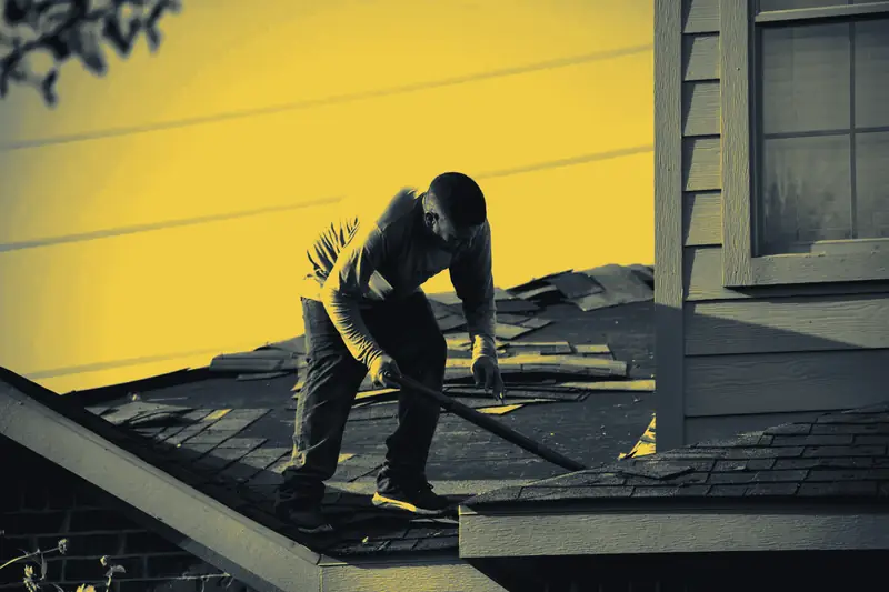 A roofer removing old shingles along a ridge