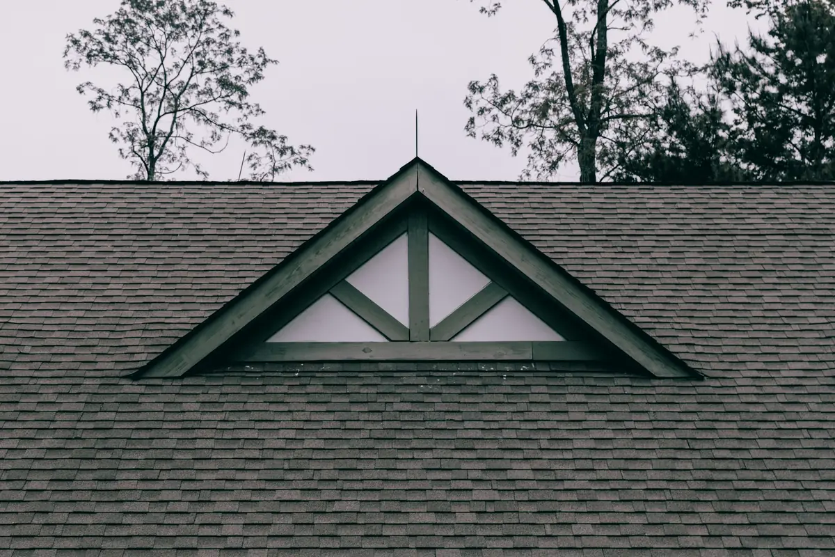 Close view of a shingled gable with a vent under an overcast sky